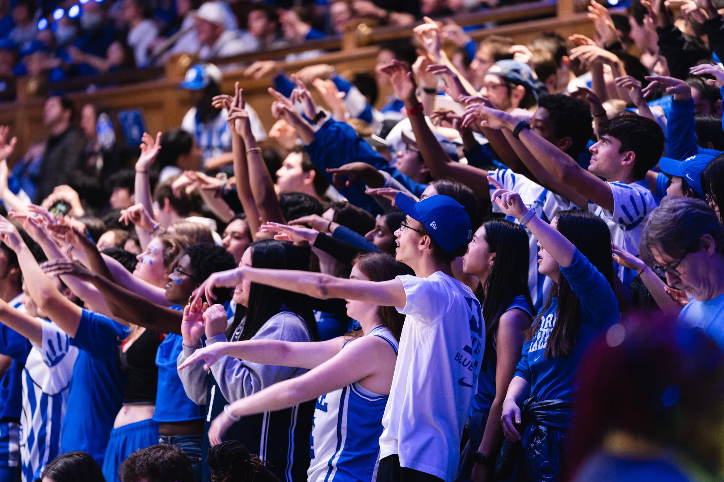 A packed student section standing with arms raised during a game